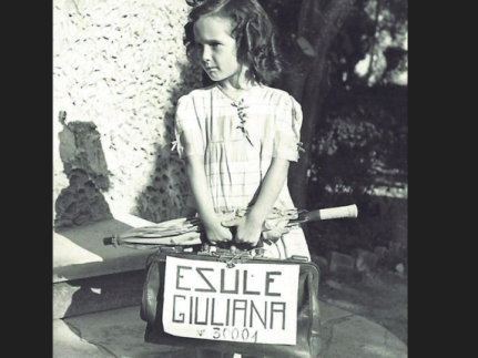 La foto la conoscete tutti. C’è una bambina, bellissima ma triste, ha i boccoli, un abitino elegante, tra le mani tiene un ombrello e una valigia grande metà di lei su cui campeggia la scritta: “Esule Giuliana”. L’immagine è divenuta il simbolo dell’esodo. La bambina si chiama Egea e aveva 5 anni e nel luglio del 1946 si stava preparando con la mamma a lasciare Pola assieme ad altri 30mila italiani. Il papà, prelevato dai partigiani di Tito, era sparito nel nulla. Lo zio Alfonso, pochi giorni prima della forzata partenza dall’Istria aveva chiesto ad un fotografo di scattare l’immagine simbolo per non dimenticare mai il dramma dell’esodo. Un dramma su cui per molto si è detto troppo poco, e poi si è detto pure troppo.